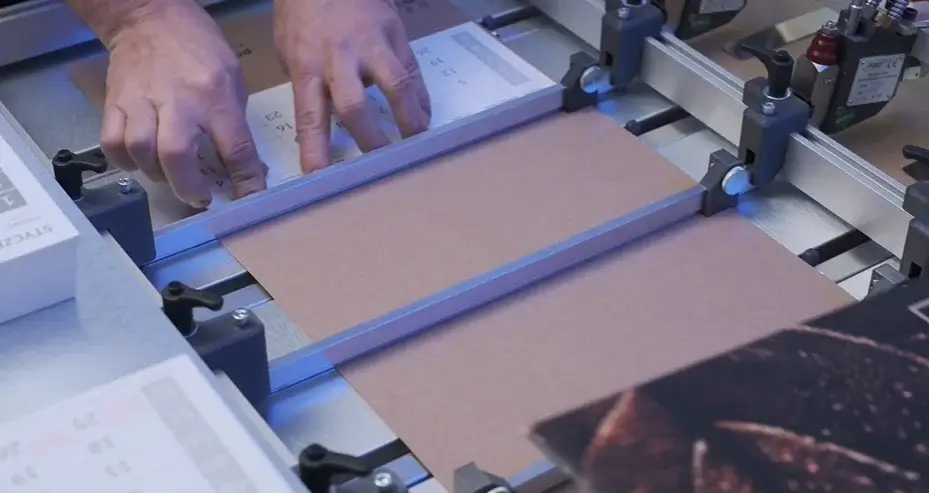 Ręce pracownika ustawiające brązowy materiał na niebieskiej ramie drukującej - CAL-One